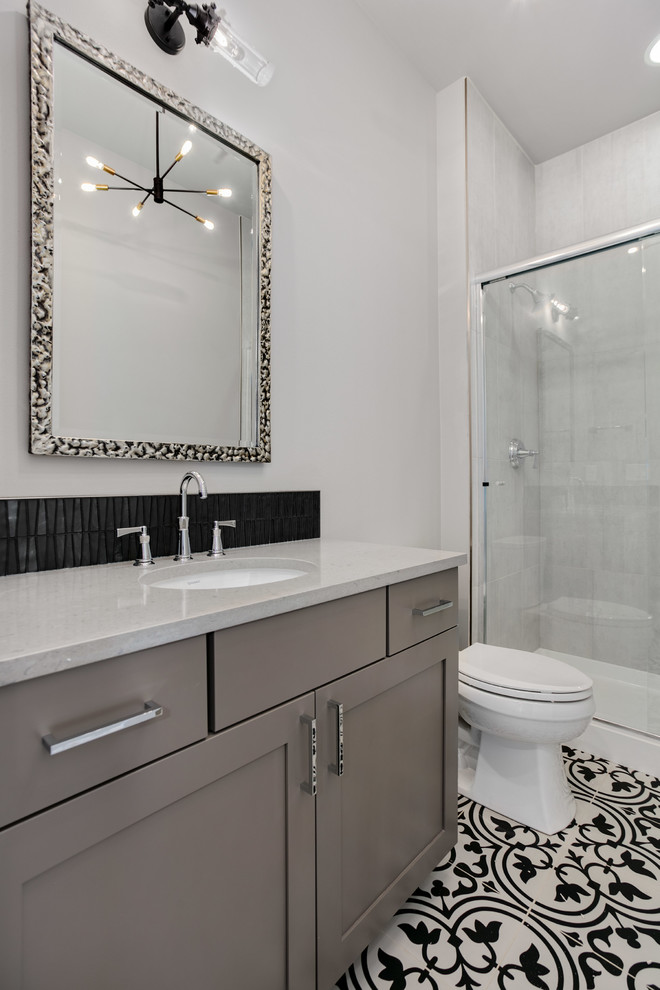 Modern inredning av ett stort badrum med dusch, med luckor med infälld panel, grå skåp, en dusch i en alkov, en toalettstol med separat cisternkåpa, svart kakel, grå väggar, ett undermonterad handfat, bänkskiva i kvarts, flerfärgat golv och dusch med skjutdörr
