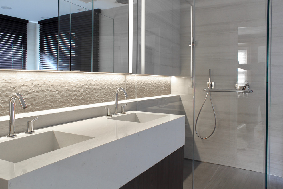 This is an example of a medium sized contemporary ensuite bathroom in New York with glass-front cabinets, dark wood cabinets, a freestanding bath, a built-in shower, a one-piece toilet, beige tiles, ceramic tiles, beige walls, ceramic flooring, an integrated sink, engineered stone worktops, beige floors, a hinged door and beige worktops.