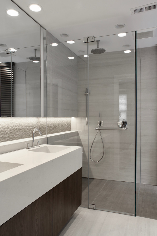 Medium sized contemporary ensuite bathroom in New York with glass-front cabinets, dark wood cabinets, a freestanding bath, a built-in shower, a one-piece toilet, beige tiles, ceramic tiles, beige walls, ceramic flooring, an integrated sink, engineered stone worktops, beige floors, a hinged door and beige worktops.