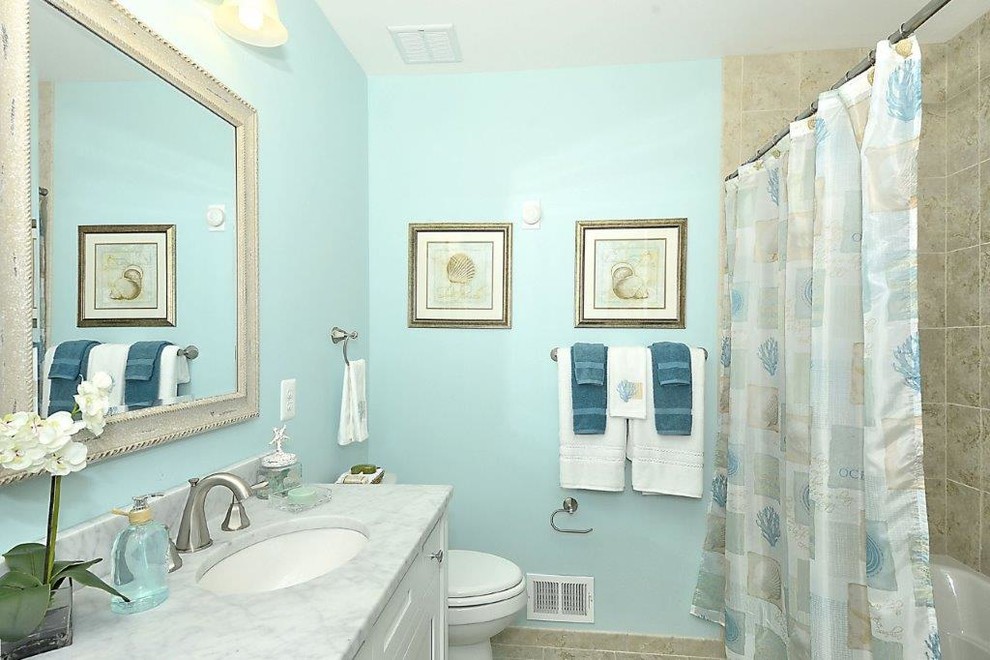 Стильный дизайн: ванная комната среднего размера в морском стиле с фасадами с утопленной филенкой, белыми фасадами, ванной в нише, душем над ванной, раздельным унитазом, бежевой плиткой, керамогранитной плиткой, синими стенами, полом из керамогранита, врезной раковиной и мраморной столешницей - последний тренд