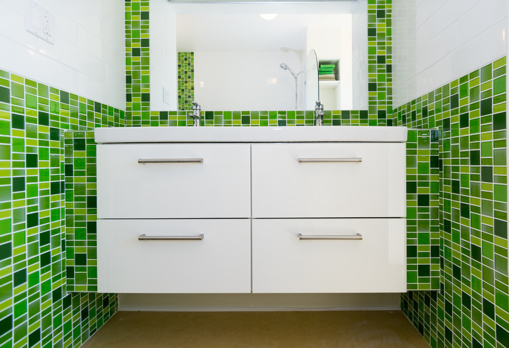 Modern inredning av ett litet en-suite badrum, med ett integrerad handfat, släta luckor, vita skåp, kaklad bänkskiva, ett platsbyggt badkar, en dusch/badkar-kombination, en toalettstol med separat cisternkåpa, grön kakel, glasskiva, vita väggar och linoleumgolv