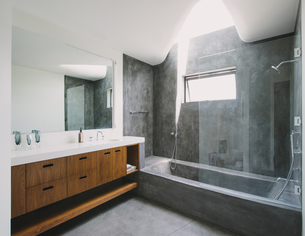 Diseño de cuarto de baño moderno con armarios con paneles lisos, puertas de armario de madera oscura, combinación de ducha y bañera, suelo de cemento y encimeras blancas