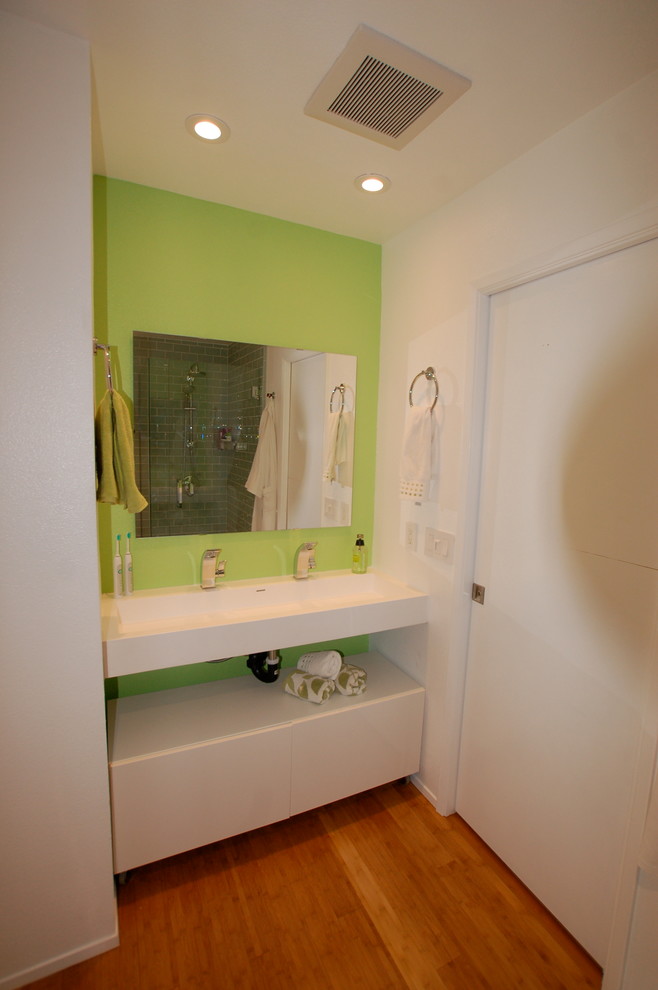 Idée de décoration pour une salle d'eau design de taille moyenne avec un placard sans porte, des portes de placard blanches, WC à poser, un carrelage vert, un carrelage métro, un mur vert, un sol en bois brun, un plan de toilette en surface solide et un lavabo encastré.