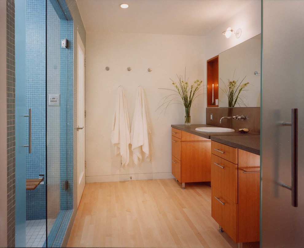 サンフランシスコにある高級な中くらいなコンテンポラリースタイルのおしゃれなマスターバスルーム (オーバーカウンターシンク、フラットパネル扉のキャビネット、中間色木目調キャビネット、御影石の洗面台、コーナー設置型シャワー、一体型トイレ	、グレーのタイル、白い壁、淡色無垢フローリング) の写真