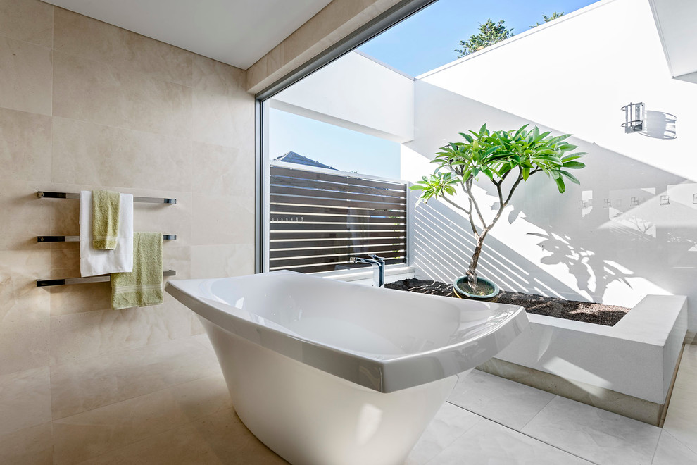 На фото: большая главная ванная комната в стиле модернизм с накладной раковиной, белыми фасадами, мраморной столешницей, отдельно стоящей ванной, бежевой плиткой, каменной плиткой, бежевыми стенами и полом из известняка с