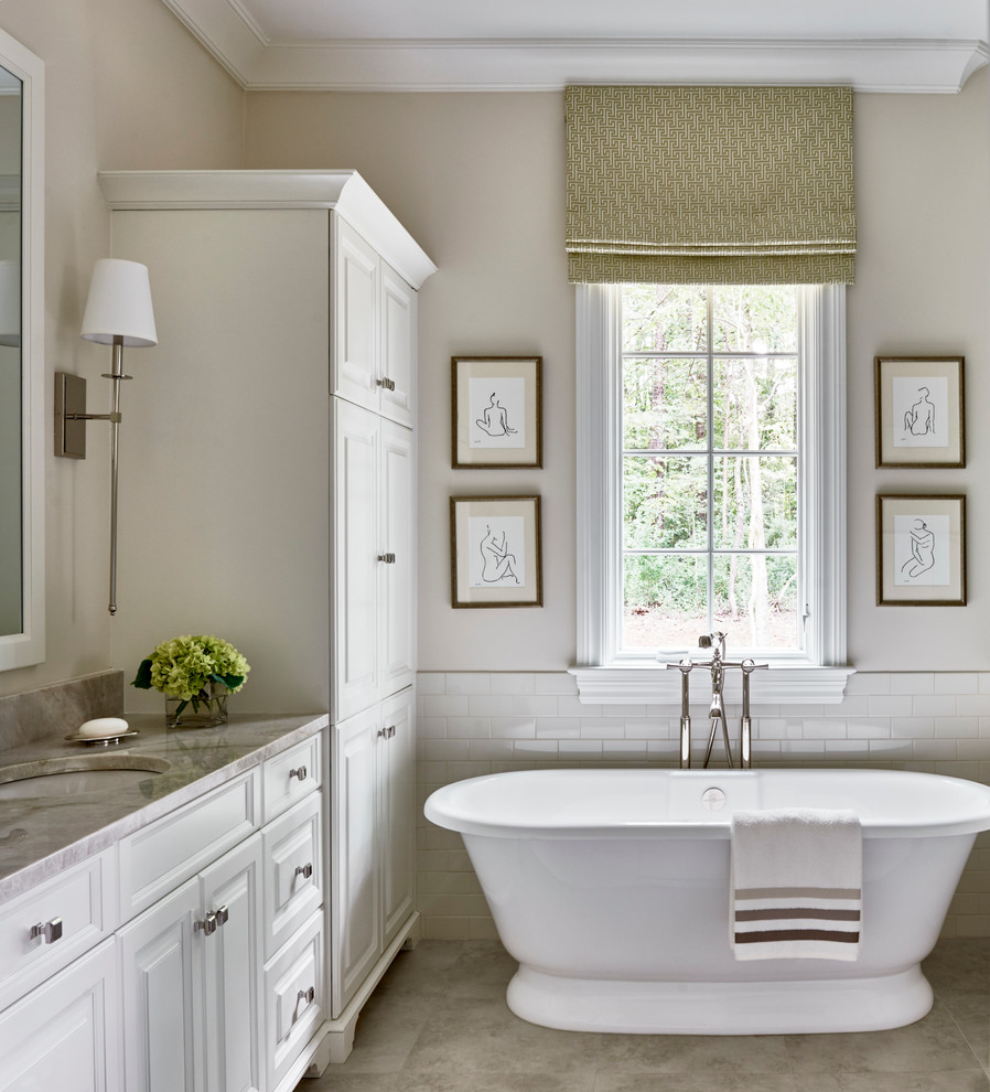 Foto på ett vintage en-suite badrum, med luckor med upphöjd panel, vita skåp, ett fristående badkar, vit kakel, tunnelbanekakel, beige väggar och ett undermonterad handfat