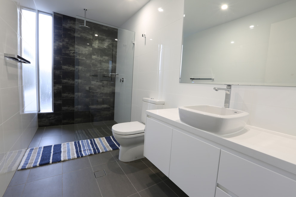 Medium sized contemporary bathroom in Sydney with flat-panel cabinets, white cabinets, a freestanding bath, a corner shower, a two-piece toilet, white tiles, porcelain tiles, white walls, cement flooring, a vessel sink, solid surface worktops, brown floors and a hinged door.