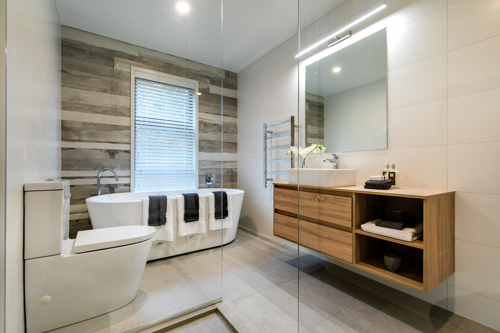 Modernes Badezimmer En Suite mit flächenbündigen Schrankfronten, hellbraunen Holzschränken, freistehender Badewanne, Nasszelle, Toilette mit Aufsatzspülkasten, beigen Fliesen, beiger Wandfarbe, Aufsatzwaschbecken, Waschtisch aus Holz, grauem Boden und offener Dusche in Auckland