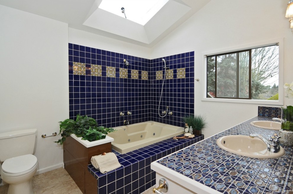 Photo of a medium sized contemporary bathroom in Seattle with white cabinets, tiled worktops, a built-in bath, a shower/bath combination, a wall mounted toilet, blue tiles, white walls, ceramic flooring and a built-in sink.