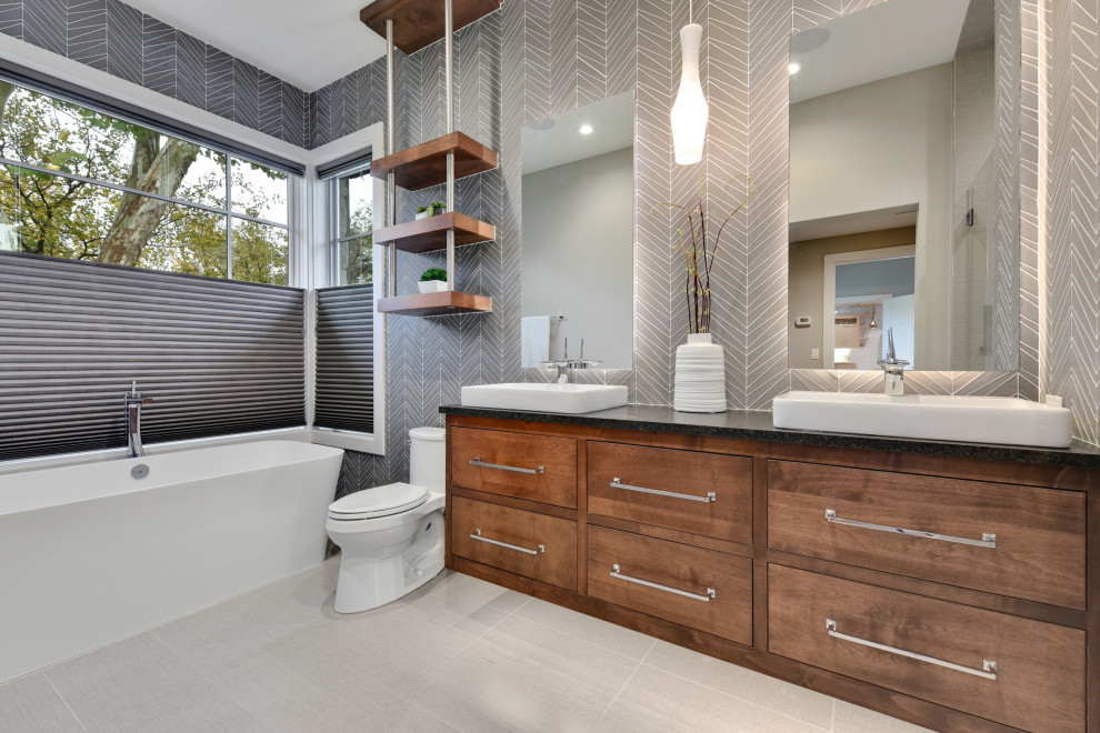 Foto di una stanza da bagno design con ante lisce, ante in legno bruno, vasca freestanding, piastrelle grigie, lavabo a bacinella, pavimento grigio, top nero e due lavabi
