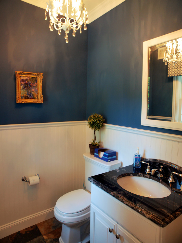 Foto på ett litet vintage toalett, med luckor med upphöjd panel, vita skåp, en toalettstol med separat cisternkåpa, blå väggar, skiffergolv och ett undermonterad handfat