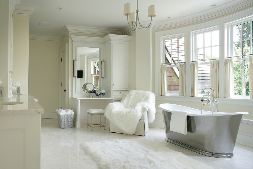 На фото: большая главная ванная комната в классическом стиле с белыми фасадами, отдельно стоящей ванной, белой плиткой, бежевыми стенами, врезной раковиной, фасадами с утопленной филенкой, мраморной столешницей, каменной плиткой и мраморным полом