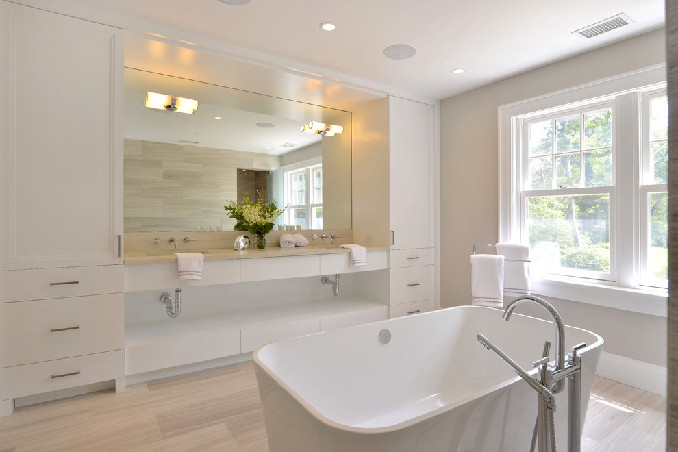 Modern inredning av ett badrum, med släta luckor, vita skåp, ett fristående badkar, beige väggar, ljust trägolv och ett undermonterad handfat