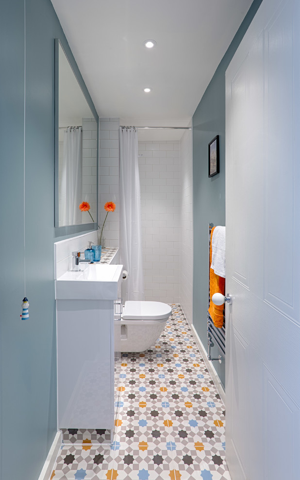 Inredning av ett modernt litet badrum med dusch, med släta luckor, vita skåp, en öppen dusch, en vägghängd toalettstol, flerfärgad kakel, keramikplattor, blå väggar, klinkergolv i keramik, ett väggmonterat handfat och kaklad bänkskiva