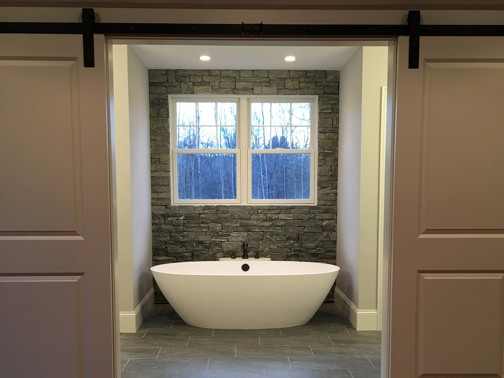 Imagen de cuarto de baño principal de estilo americano de tamaño medio con bañera exenta, baldosas y/o azulejos grises, baldosas y/o azulejos de piedra, paredes grises, suelo de baldosas de porcelana y suelo gris
