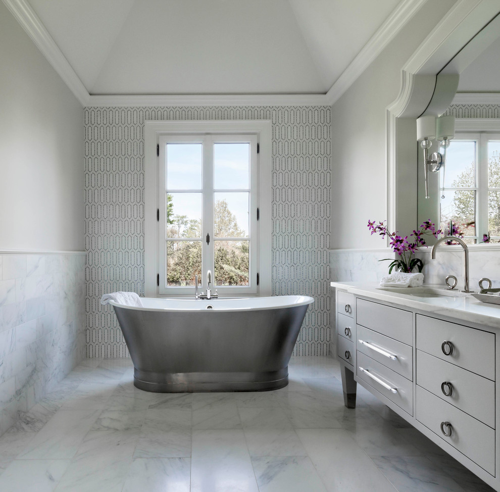 Стильный дизайн: главная ванная комната в стиле неоклассика (современная классика) с белыми фасадами, отдельно стоящей ванной, белой плиткой, белыми стенами, мраморной столешницей, плоскими фасадами и врезной раковиной - последний тренд