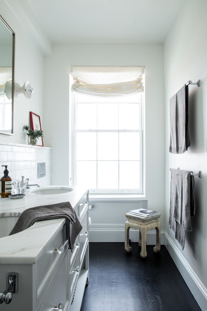 This is an example of a traditional bathroom in New York with a submerged sink, recessed-panel cabinets, white cabinets, white walls and dark hardwood flooring.