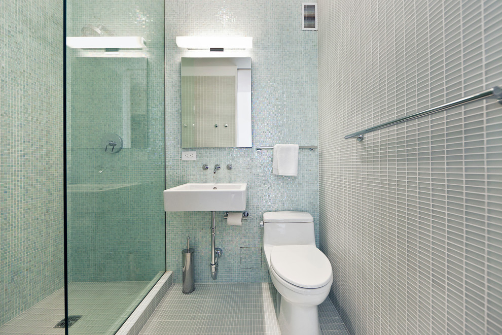 Bild på ett funkis badrum, med ett väggmonterat handfat, en dusch i en alkov, en toalettstol med hel cisternkåpa, blå kakel, glaskakel, blå väggar och mosaikgolv