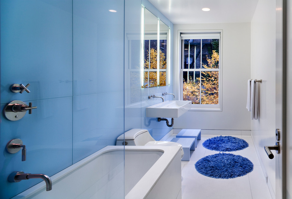 Modelo de cuarto de baño actual con bañera encastrada sin remate, combinación de ducha y bañera, paredes azules, aseo y ducha, lavabo suspendido y suelo blanco
