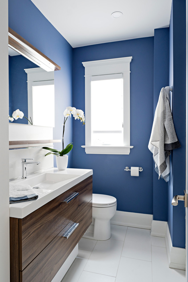 Photo of a small modern ensuite bathroom in Toronto with flat-panel cabinets, dark wood cabinets, an alcove bath, an alcove shower, a two-piece toilet, metro tiles, blue walls, an integrated sink, solid surface worktops, white floors, a shower curtain, white worktops and ceramic flooring.