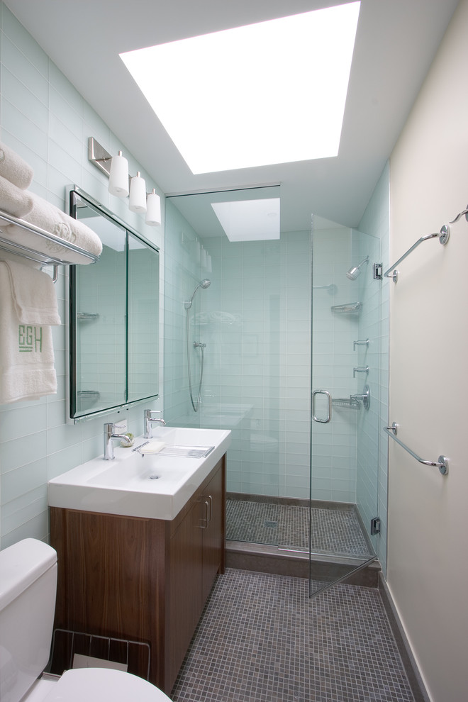 Modelo de cuarto de baño contemporáneo con lavabo de seno grande, puertas de armario de madera en tonos medios, ducha doble, sanitario de dos piezas, baldosas y/o azulejos azules, baldosas y/o azulejos de vidrio y armarios con paneles lisos