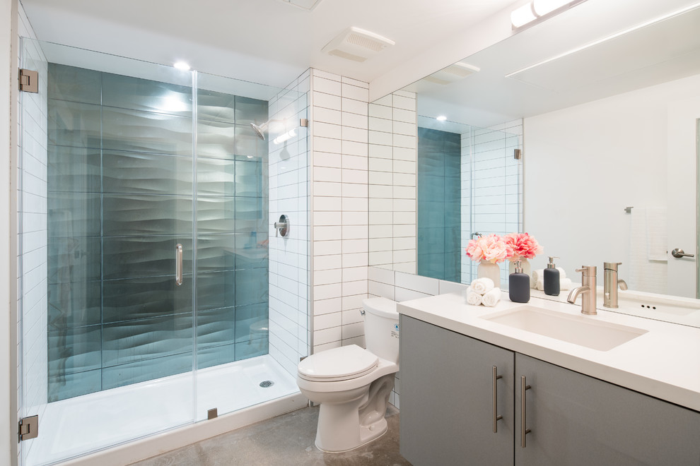 Foto på ett mellanstort funkis vit badrum med dusch, med släta luckor, en toalettstol med hel cisternkåpa, tunnelbanekakel, vita väggar, betonggolv, ett undermonterad handfat, bänkskiva i kvarts, grå skåp, en dusch i en alkov, vit kakel, grått golv och dusch med gångjärnsdörr