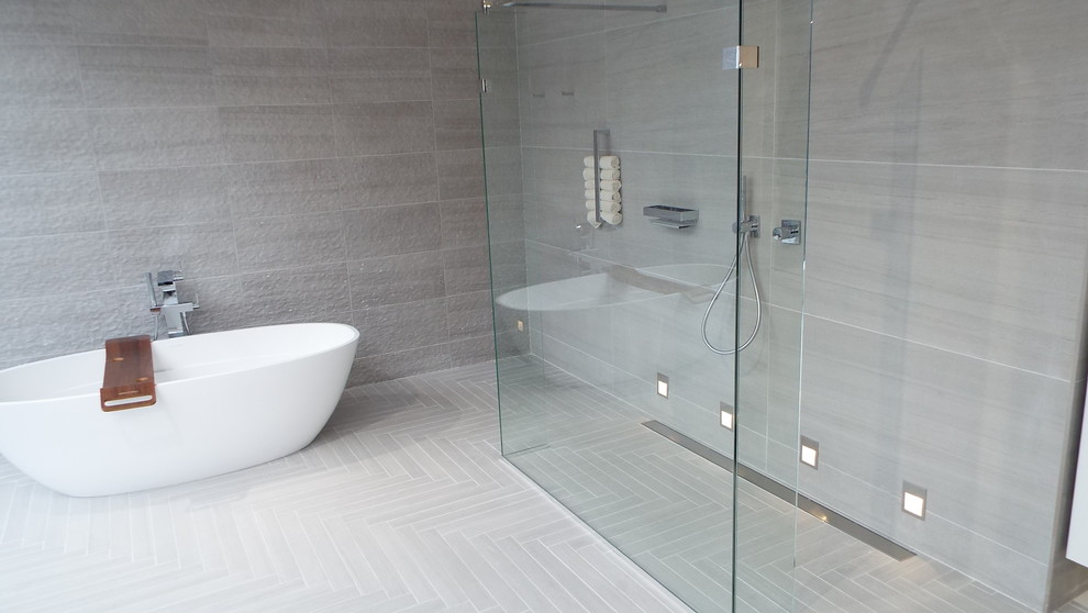 This is an example of a contemporary bathroom in London with glass-front cabinets, white cabinets, a freestanding bath, a walk-in shower, a wall mounted toilet, grey tiles, porcelain tiles, grey walls, porcelain flooring, an integrated sink, engineered stone worktops, grey floors, an open shower and white worktops.