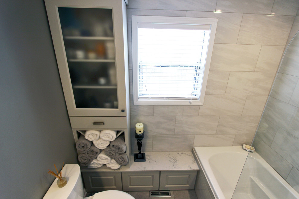 Exempel på ett litet klassiskt en-suite badrum, med luckor med upphöjd panel, grå skåp, ett badkar i en alkov, en dusch i en alkov, en toalettstol med separat cisternkåpa, grå kakel, porslinskakel, grå väggar, klinkergolv i porslin, ett undermonterad handfat, bänkskiva i akrylsten, grått golv och dusch med gångjärnsdörr