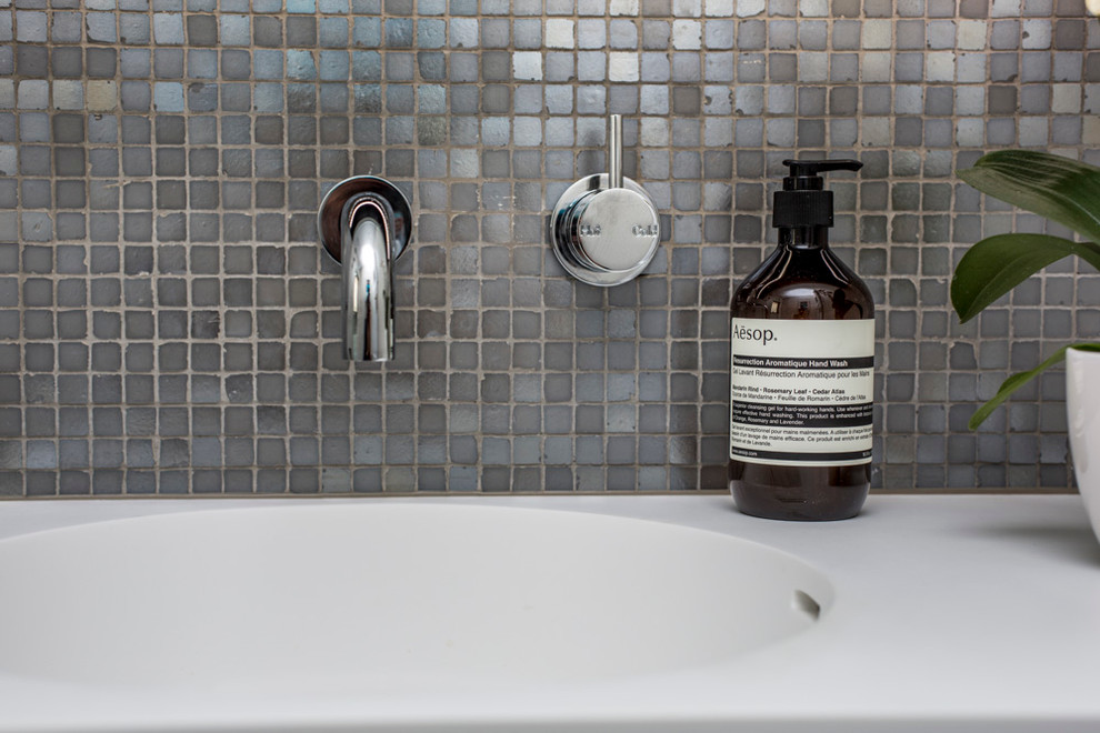 Foto på ett litet minimalistiskt badrum, med ett väggmonterat handfat, bänkskiva i akrylsten, en öppen dusch, en toalettstol med hel cisternkåpa, grå kakel, mosaik, vita väggar, klinkergolv i porslin, grått golv och med dusch som är öppen