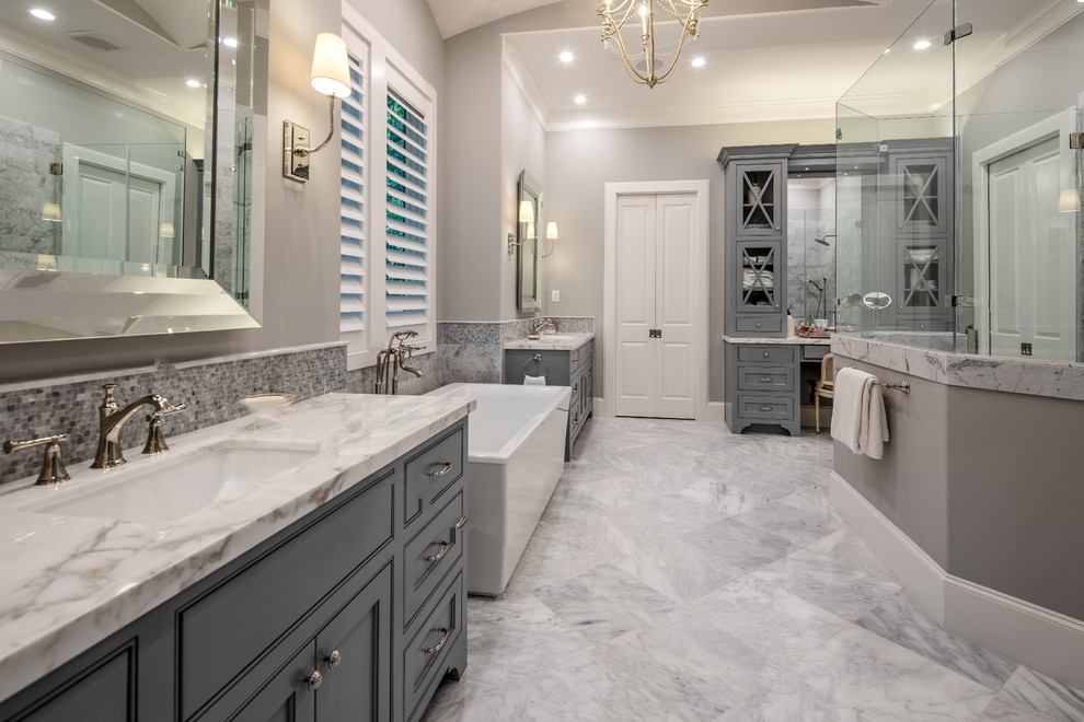 Klassisk inredning av ett mycket stort vit vitt en-suite badrum, med luckor med profilerade fronter, grå skåp, ett fristående badkar, grå kakel, grå väggar, ett undermonterad handfat, grått golv, en dubbeldusch, marmorkakel, marmorgolv, marmorbänkskiva och dusch med gångjärnsdörr