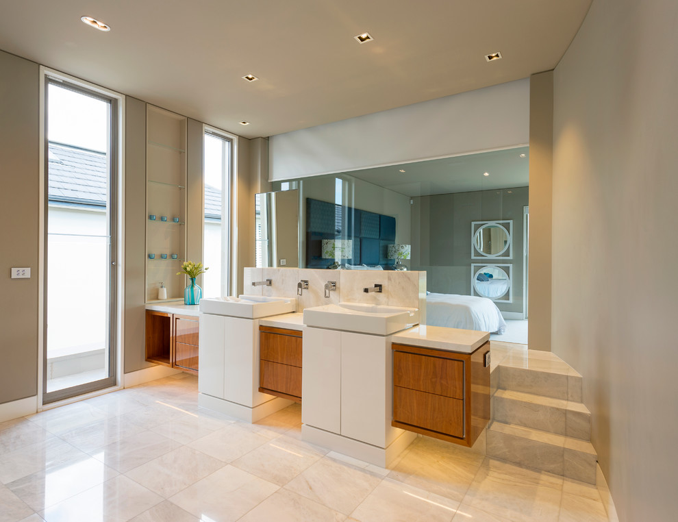 Imagen de cuarto de baño principal minimalista con armarios tipo mueble, puertas de armario de madera clara, baldosas y/o azulejos de piedra, encimera de mármol, bañera encastrada y lavabo sobreencimera