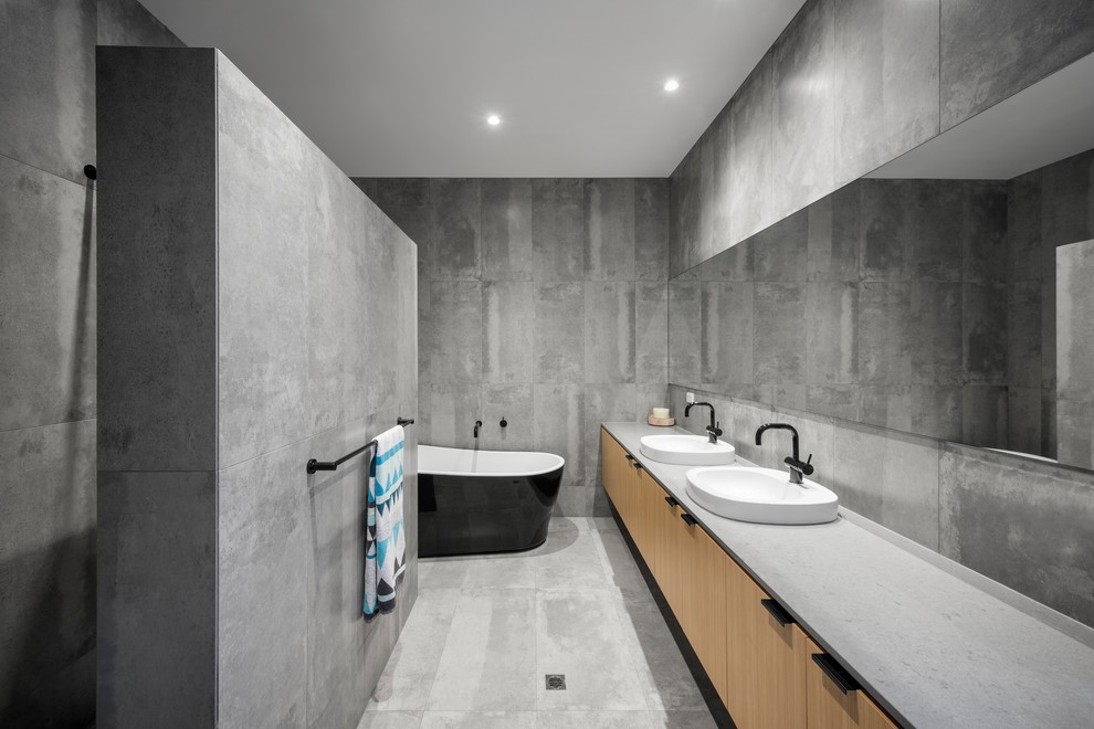 Foto på ett mellanstort funkis en-suite badrum, med släta luckor, skåp i ljust trä, ett fristående badkar, en öppen dusch, grå kakel, keramikplattor, klinkergolv i keramik, ett nedsänkt handfat, bänkskiva i betong, grå väggar, grått golv och med dusch som är öppen
