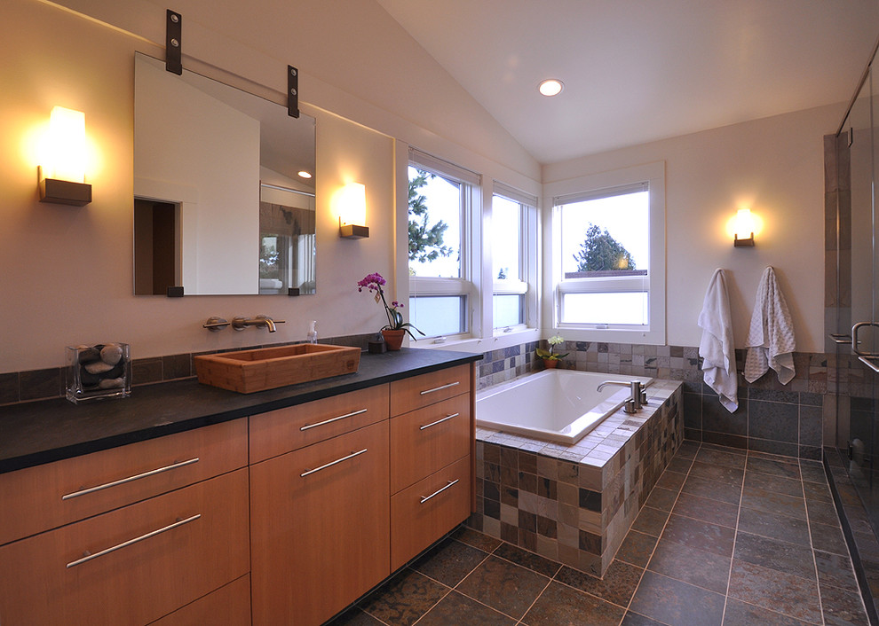 Photo of a large contemporary ensuite bathroom in Seattle with a vessel sink, flat-panel cabinets, medium wood cabinets, soapstone worktops, a corner bath, an alcove shower, a one-piece toilet, grey tiles, stone tiles, white walls and slate flooring.