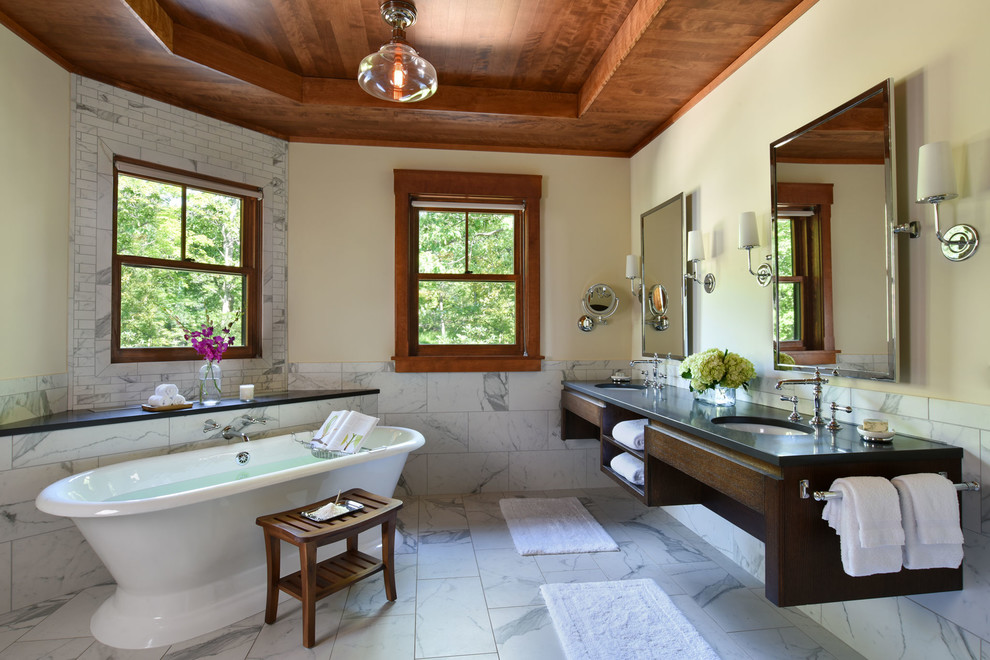 Cette photo montre une salle de bain principale craftsman en bois foncé avec un placard sans porte, une baignoire indépendante, un carrelage blanc, un mur beige et un lavabo encastré.
