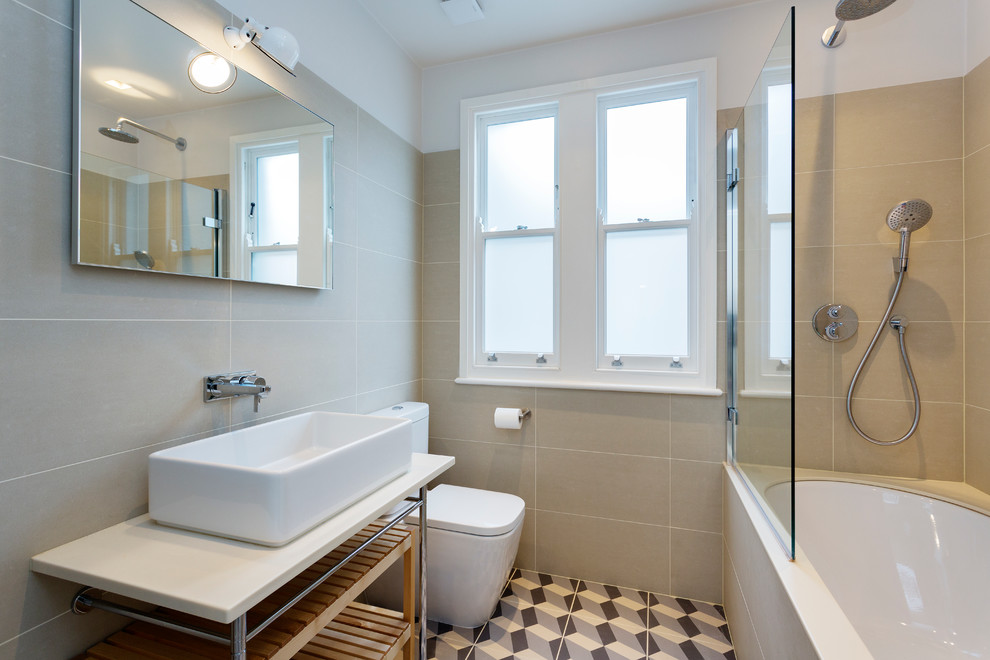 Foto på ett mellanstort vintage badrum, med ett undermonterat badkar, en dusch/badkar-kombination, en toalettstol med separat cisternkåpa, beige kakel, vita väggar och ett fristående handfat