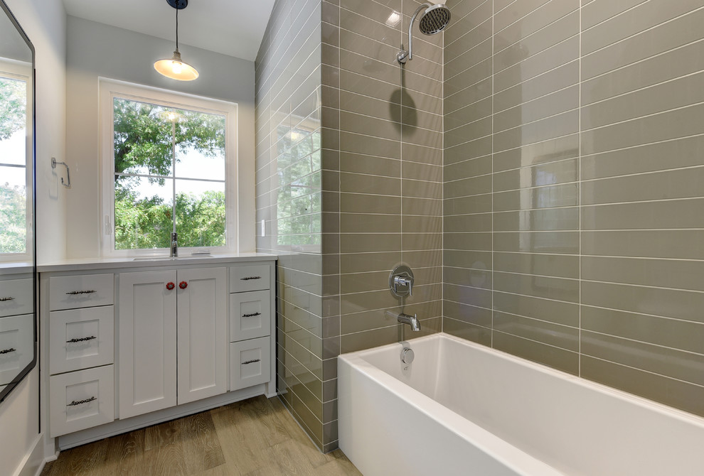 Small modern shower room bathroom in Austin with shaker cabinets, white cabinets, an alcove bath, an alcove shower, beige tiles, porcelain tiles, white walls, light hardwood flooring, a submerged sink and solid surface worktops.
