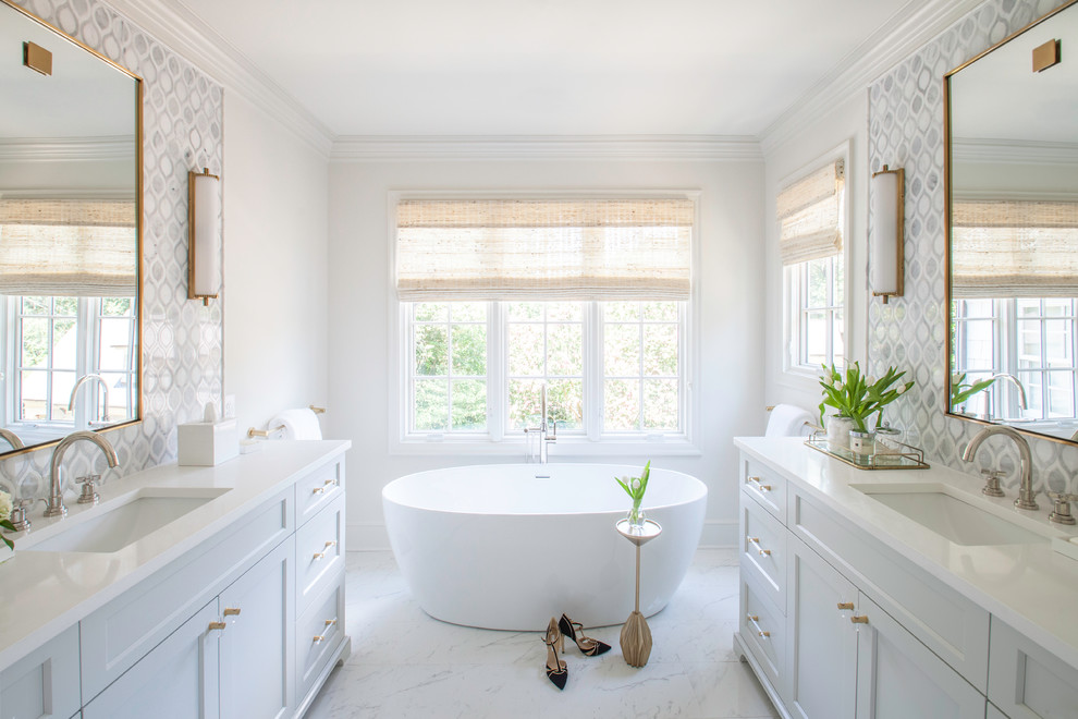 Cette image montre une salle de bain traditionnelle avec un placard à porte shaker, des portes de placard blanches, une baignoire indépendante, un carrelage blanc, un mur blanc, un lavabo encastré et un sol blanc.