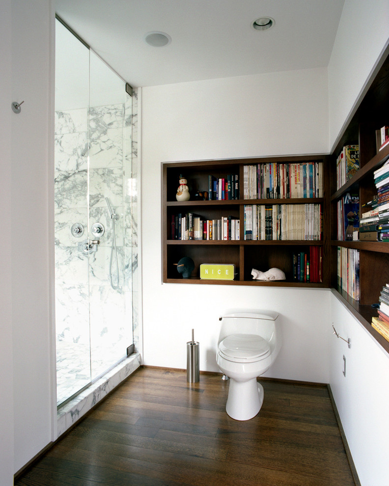 Modelo de cuarto de baño principal, actual, grande, con sanitario de una pieza, paredes blancas, suelo de madera oscura, armarios abiertos, puertas de armario de madera en tonos medios, ducha empotrada y losas de piedra
