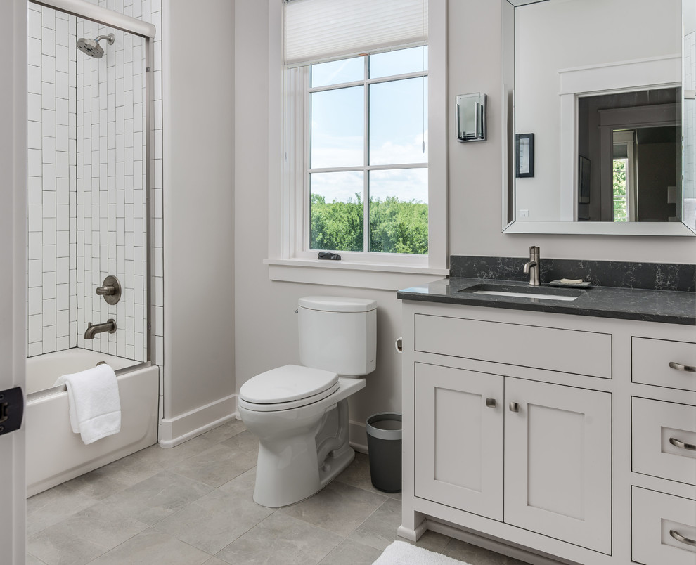 Photo of a traditional shower room bathroom in Nashville with beaded cabinets, white cabinets, a built-in bath, a shower/bath combination, a two-piece toilet, white tiles, porcelain tiles, grey walls, ceramic flooring, a submerged sink, engineered stone worktops, grey floors, a sliding door and black worktops.
