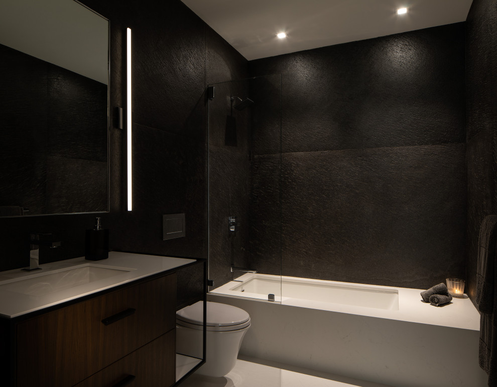 Bild på ett funkis vit vitt badrum, med släta luckor, vita skåp, ett undermonterat badkar, svart kakel, skifferkakel, klinkergolv i porslin och bänkskiva i kvarts