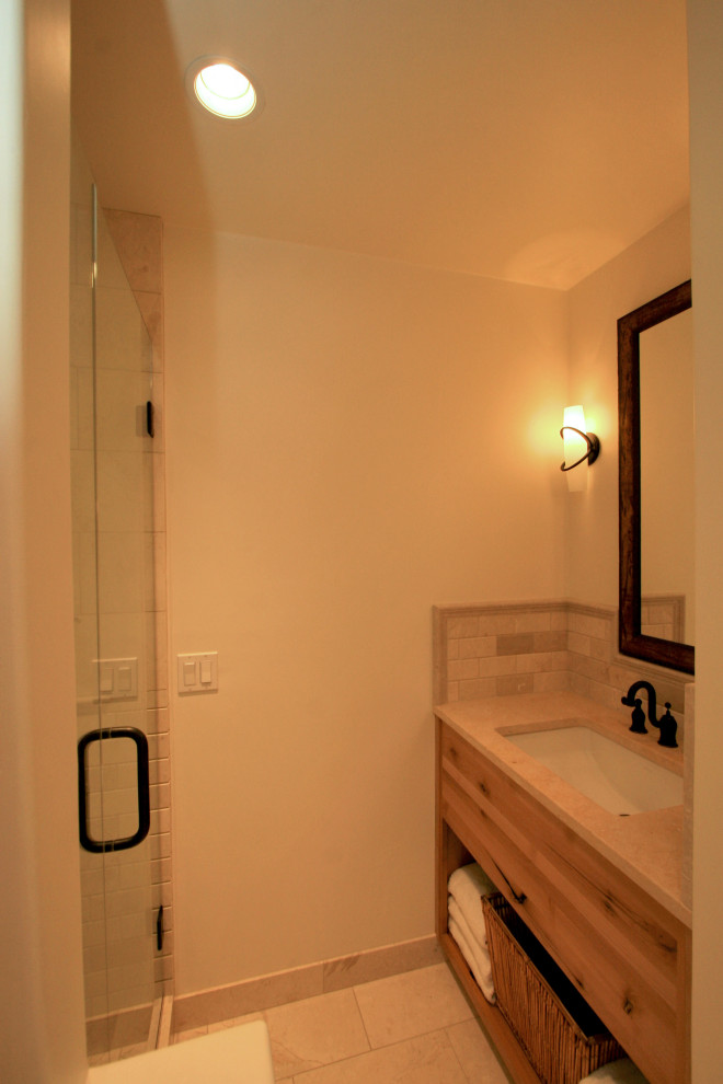 Стильный дизайн: главная ванная комната среднего размера в стиле кантри с плоскими фасадами, фасадами цвета дерева среднего тона, душем в нише, раздельным унитазом, бежевой плиткой, плиткой из травертина, белыми стенами, полом из известняка, врезной раковиной, столешницей из искусственного камня, бежевым полом, душем с распашными дверями и бежевой столешницей - последний тренд