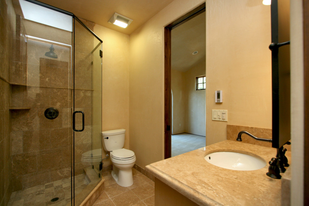 Exempel på ett stort medelhavsstil beige beige en-suite badrum, med luckor med infälld panel, skåp i mörkt trä, ett platsbyggt badkar, en dusch i en alkov, en toalettstol med separat cisternkåpa, beige kakel, travertinkakel, beige väggar, travertin golv, ett undermonterad handfat, bänkskiva i kalksten, beiget golv och dusch med gångjärnsdörr