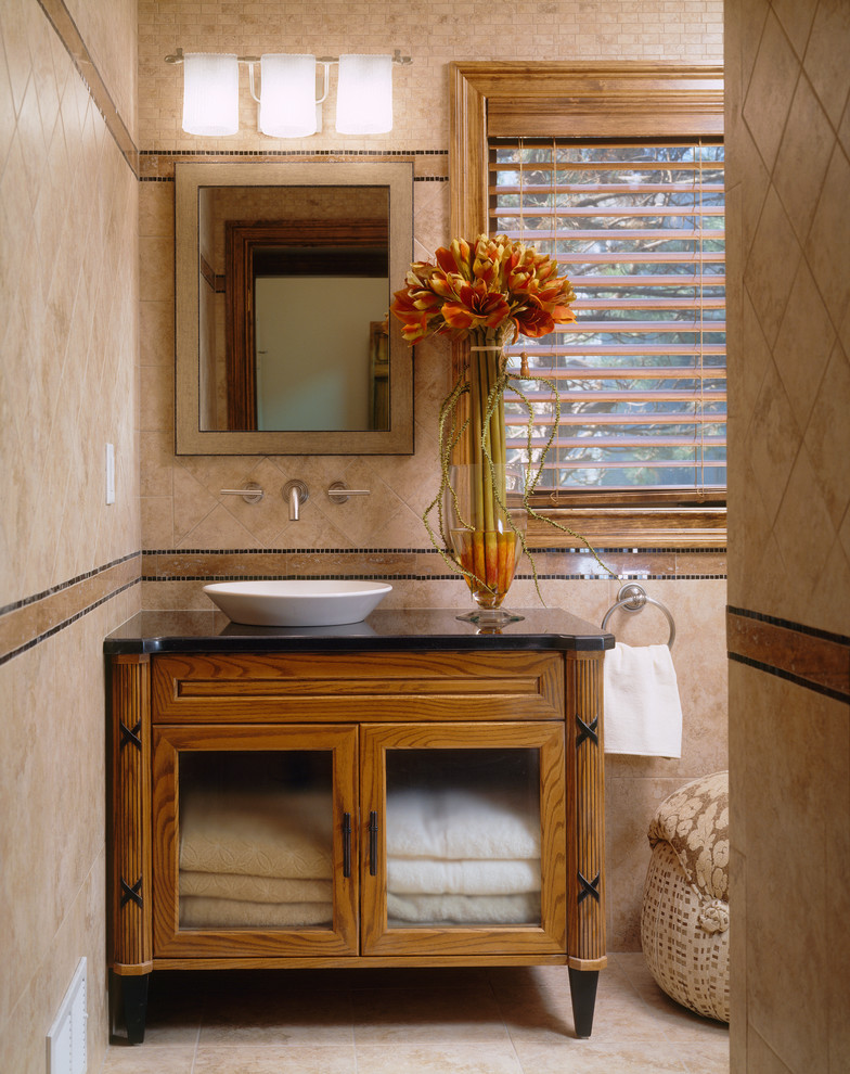 Cette photo montre une salle de bain chic en bois brun de taille moyenne avec une vasque, un placard à porte vitrée, WC à poser, un carrelage marron, des carreaux de porcelaine, un mur marron, un sol en carrelage de porcelaine et un plan de toilette en granite.