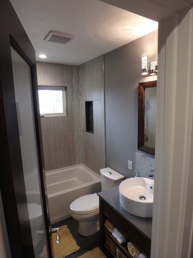 Idéer för ett mellanstort modernt badrum, med möbel-liknande, skåp i mellenmörkt trä, ett badkar i en alkov, en dusch/badkar-kombination, en toalettstol med separat cisternkåpa, grå kakel, porslinskakel, grå väggar, klinkergolv i porslin, ett fristående handfat, bänkskiva i akrylsten och grått golv