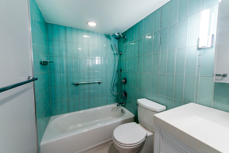 Пример оригинального дизайна: ванная комната среднего размера в современном стиле с фасадами островного типа, белыми фасадами, полновстраиваемой ванной, душем над ванной, раздельным унитазом, бежевой плиткой, плиткой из листового стекла, зелеными стенами, полом из керамогранита, душевой кабиной, врезной раковиной и столешницей из дерева