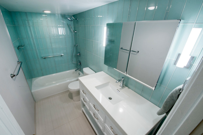 Exemple d'une salle d'eau tendance de taille moyenne avec un mur bleu, un sol en carrelage de porcelaine, un placard avec porte à panneau encastré, des portes de placard blanches, une baignoire en alcôve, un combiné douche/baignoire, WC séparés, un carrelage bleu, mosaïque, un lavabo intégré et un plan de toilette en surface solide.