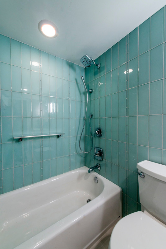 Bild på ett mellanstort funkis badrum med dusch, med möbel-liknande, vita skåp, ett undermonterat badkar, en dusch/badkar-kombination, en toalettstol med separat cisternkåpa, beige kakel, glasskiva, gröna väggar, klinkergolv i porslin, ett undermonterad handfat och träbänkskiva