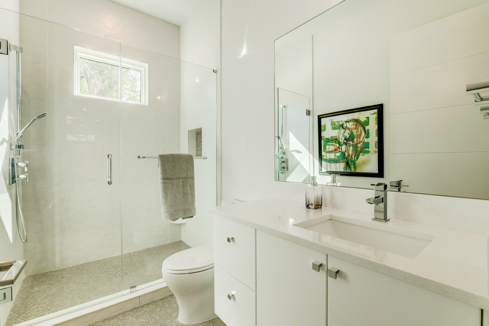 Example of a minimalist 3/4 beige tile and ceramic tile ceramic tile and beige floor bathroom design in Tampa with flat-panel cabinets, white cabinets, a one-piece toilet, white walls, an undermount sink, quartz countertops and white countertops
