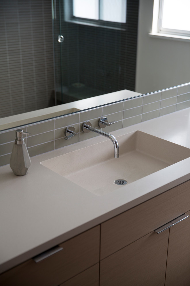 Exemple d'une salle de bain moderne de taille moyenne avec un placard à porte plane, un carrelage gris, des carreaux de porcelaine, un lavabo intégré et un plan de toilette en surface solide.