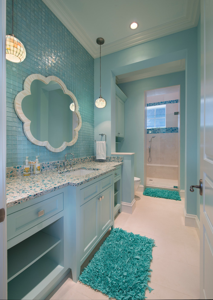 マイアミにあるビーチスタイルのおしゃれな子供用バスルーム (アンダーカウンター洗面器、落し込みパネル扉のキャビネット、青いキャビネット、青いタイル、ガラスタイル、青い壁、セラミックタイルの床) の写真
